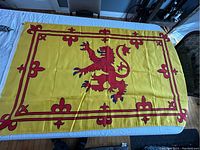 Photo showing the full Scotland Royal Banner Flag laid flat on a table. The yellow field with the red lion rampant and red borders with fleur-de-lis is clearly visible.
