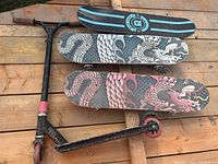 Three skateboards with dragon scale style graphics and black scooter with red wheels on wooden surface
