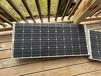 One Shell Solar SQ80 solar panel showing front surface with 36 black monocrystalline cells in a 6x6 grid, silver trim frame, placed on wooden deck.