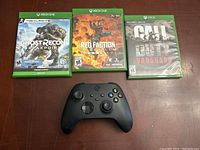 Photo showing three Xbox One game cases: Ghost Recon Breakpoint, Red Faction Guerrilla Re-Mars-tered, Call of Duty Vanguard, along with a black Xbox wireless controller.