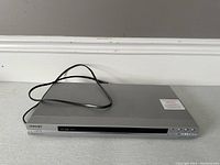 Full view of the silver Sony DVD player with power cord attached showing the front panel and disc tray.