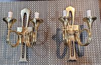 Pair of brass wall-mounted candle holders placed side by side on a textured surface.