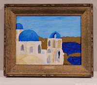 Framed painting showing white buildings with blue domes and sea in bright colors.