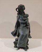 Front photo of signed statue depicting a seated woman holding a child. Detailed flowing robes and hair. Dark textured material.