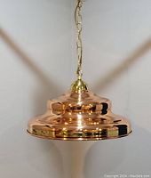 Front view of the polished copper hanging lamp suspended by a brass chain, showing the smooth reflective surface and tiered circular design.