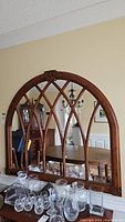 Full view of the wood framed arched mirror on the wall with dining room visible in reflection.
