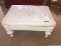 Front angle of white faux leather bench showing worn and stained cushion with four rounded legs.