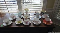 Twelve assorted bone china teacup & saucer pairs arranged on wooden table