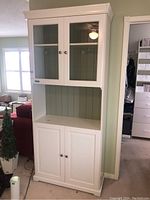 Front view of white wood cabinet with glass doors on top, open middle shelf with green back, lower solid doors.