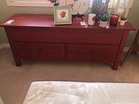 Front view of red wooden credenza with some decorative items on top, showing two drawers and rectangular shape.