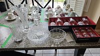 Photo of crystal decanter with stopper, small Wedgwood bowl, crystal vase, glass vase, and boxed Cristal D'arques wine and shot glasses on granite countertop
