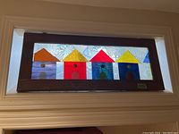 Full view of stained glass art panel with colorful houses in wooden frame.