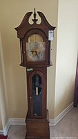 Full frontal view of Forestville grandmother clock showing wood case, arched bonnet, clock face, and packaging tag.
