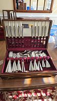 Wood case open showing top row of 12 dinner knives with fluted gold-accented handles and bottom row of assorted flatware in burgundy velvet lining