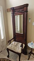 Full view front of dark brown wooden hall tree showing mirror, arm seat and feet