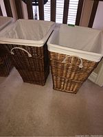 Two wicker laundry hampers side by side, showing the cotton liners and white plastic handles on the sides.