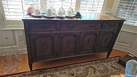 Front view of wooden vintage sideboard with detailed paneled doors and some glassware and cups on top.