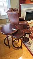 Three wooden nesting tables arranged in front of brown leather chair and fireplace, showing overall condition and size differences