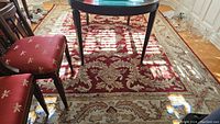 Full view of the red and beige patterned synthetic blend area rug under a table with chairs
