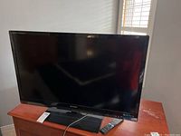 Front view of Sharp Aquos Quattron 40 inch TV on stand with remote control on base.