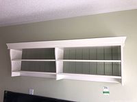 Front view of white wall shelf with two shelves and green backing mounted on wall.