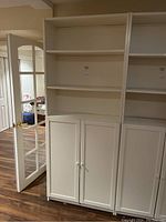 Front view of white shelving unit showing three adjustable shelves and lower cabinet with closed double doors.