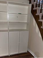 Side view of the white shelving unit with upper adjustable shelves and lower cabinet doors under staircase.