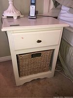 Front view of the side table showing drawer with brass knob and lower wicker basket in open storage cubby.