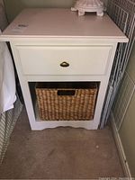 Front view of white side table showing drawer with metal handle and wicker basket in lower shelf.