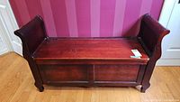 Front view of dark wood storage bench with sleigh ends, seat shows scratches, solid panel legs and panels on front storage door