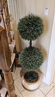 Full view of the faux topiary showing the two sphere foliage clusters, twisted faux wood stem, and round ceramic base with wicker trim.