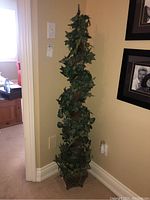 Full view of tall faux ivy leaf topiary plant in corner showing height and base planter.