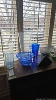 Wide shot of six art glass pieces on a table in front of window blinds