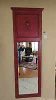 Full view of the tall, narrow vertical wall mirror with red ornate wooden frame and beveled glass reflection.
