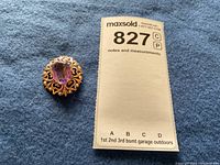 Brooch positioned next to lot tag on blue cloth background