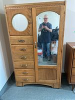 Full front view of wooden armoire showing six drawers on left and two mirrored doors on right, including person reflection in large mirror.