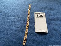 Bracelet laid flat on blue fabric with MaxSold tag showing lot number 825