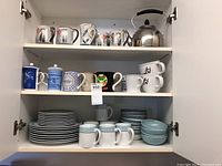 Cabinet shelves showing all dishware including striped plates, bowls, mugs, and kettle.