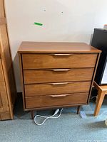 Front view of a wooden four drawer dresser with integrated carved handles and minor surface wear.