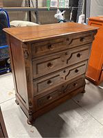Front right angle view showing solid wood dresser with four drawers, ornate carved details on corners, wooden knob handles, and surface wear.