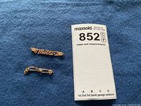 Photo showing the 14K gold Mother insignia along with the partial 18K gold chain segment on a blue background next to the lot tag.