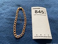 Full view of gold curb link bracelet laid out on fabric with lot number card