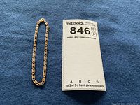 Gold bracelet laid flat on blue cloth next to a MaxSold lot ticket