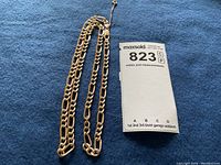 Full view of folded figaro chain on blue background with MaxSold tag visible