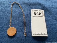 Full view of chain and round locket beside MaxSold notes and measurement card