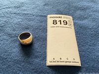 Ring on blue fabric next to MaxSold note card showing lot number