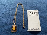 Full view of pendant and chain on blue background with lot tag