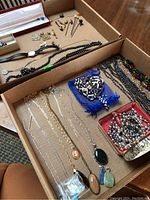 Overview of various necklaces, chains with pendants, beaded bracelets, and filigree earring set in a blue bag.