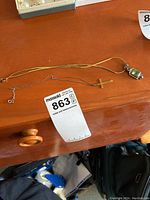 Overview of two necklaces on wooden surface: 14K gold cross pendant on a fine chain and sterling silver pendant with green stones on a gold-tone chain.