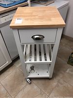 Full view of kitchen cart showing wooden top, drawer, slatted shelf and casters